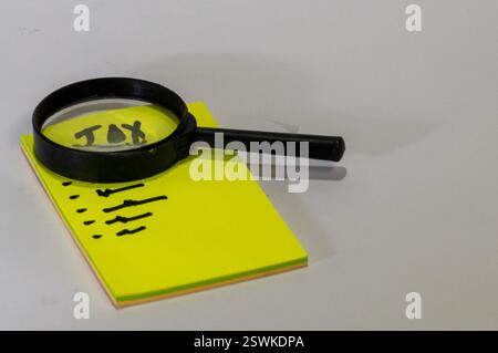 Vor dem Block befindet sich ein gelber Notizblock mit dem Wort „TAX“ auf dem oberen Blatt, gefolgt von einem Pfeil nach unten. Stockfoto