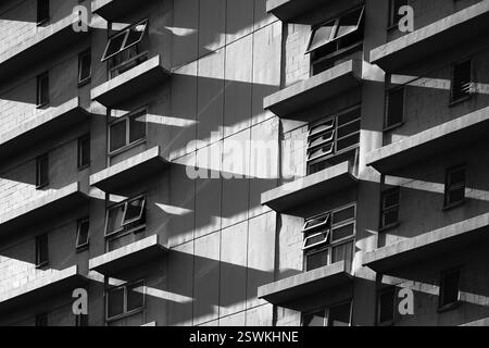 Kontrastreiche Kunstabstraktion von Licht und Schatten, die an Fenstern und Vorsprüngen eines Wohnblocks mit Argyle-Diamanten Muster kreiert Stockfoto