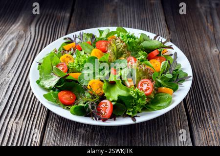 Bunte Salatmischung aus frischem Gemüse und Kirschtomaten auf einem weißen Teller über einem rustikalen Holzhintergrund. Inspiration für das kulinarische Styling Stockfoto