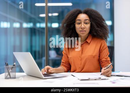 Porträt einer ernsthaften, selbstbewussten Geschäftsfrau am Arbeitsplatz. Frau, die sich in die Kamera konzentriert, einen Vertrag unterzeichnet und Steuerformulare ausfüllt. Finanzier im Büro, der Papierkram macht. Stockfoto