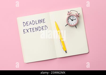 Textfrist verlängert in Notizbuch, Stift und Wecker auf rosa Hintergrund, Draufsicht Stockfoto