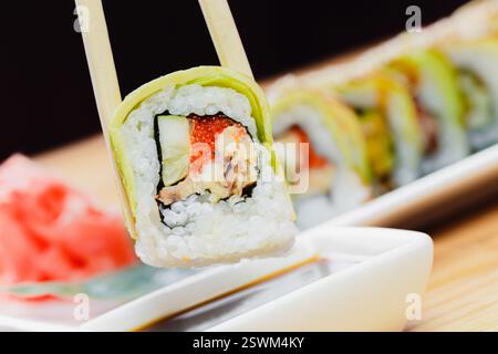 Sushi-Rollenstück, das mit Stäbchen in Nahaufnahme gehalten wird Stockfoto