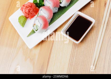 Frische Sushi-Scheiben ordentlich auf einem Holztisch mit Sojasauce und Beilagen Stockfoto