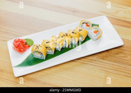 Sushi-Platte kunstvoll mit gelben Brötchen und eingelegtem Ingwer auf einem Holztisch angeordnet Stockfoto