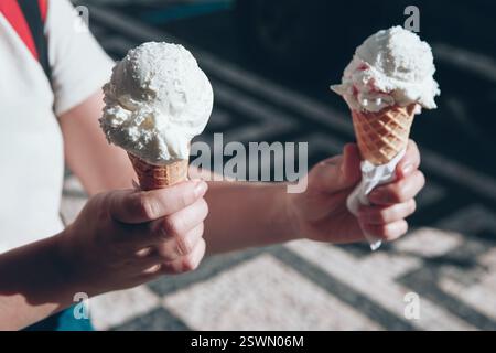 Mädchen, das zwei Eiskegel in der Hand hält, jede mit einem Löffel weißem Eis belegt. Süßes Sommervergnügen, perfekt für einen sonnigen Tag Stockfoto
