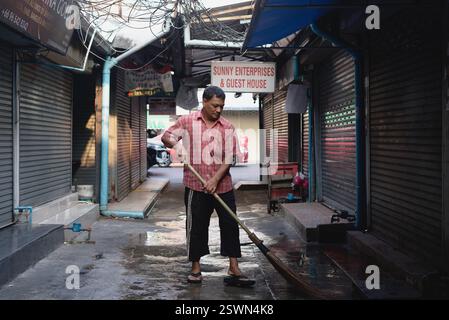 Ein ethnischer Nepalese aus Myanmar, Angestellter in einem Restaurant im indischen Viertel Pahurat, Bangkok, Thailand, der von seinem Arbeitsplatz aus die Straße einfegt Stockfoto