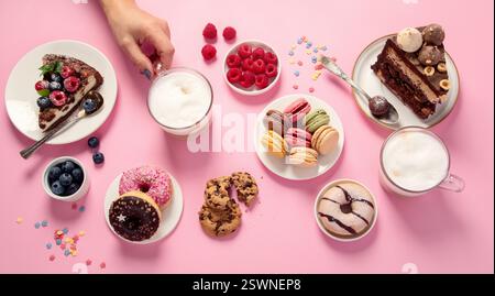 Verschiedene Kekse, Donuts, Kuchen, Käsekuchen und Kaffeetassen auf rosa Hintergrund. Köstlicher Nachtisch. Draufsicht, flach Stockfoto