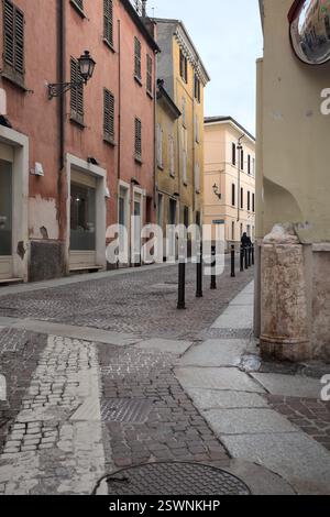 Kopfsteinpflasterstraße teilweise im Schatten mit Schaufensterfenstern an einem bewölkten Tag in einer italienischen Stadt Stockfoto