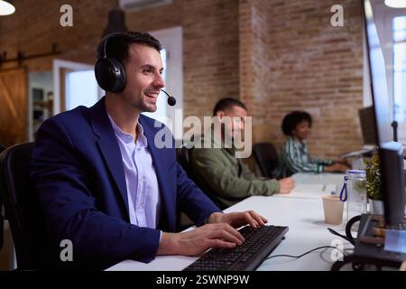 Lächelnder männlicher Callcenter-Agent, der im Büro am Computer arbeitet Stockfoto