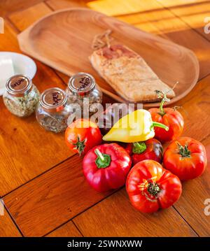 Farbenfrohe frische Produkte mit Kräutern und Brot auf einer rustikalen Holzplatte. Stockfoto