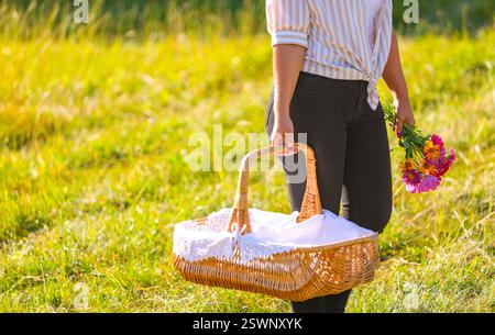 Heller, sonniger Tag mit einer Frau mit Blumen und einem gewebten Korb im Freien. Stockfoto
