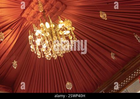 Flacher Blick auf einen raffinierten Kristalllüster, der von der roten Decke eines Zeltes in marsa alam, ägypten hängt, und schafft ein luxuriöses Ambiente Stockfoto