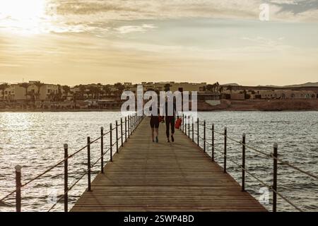 Zwei Taucher gehen nach einem Tauchgang zurück an die Küste und tragen ihre Ausrüstung auf einem hölzernen Steg bei Sonnenuntergang in marsa alam, ägypten Stockfoto