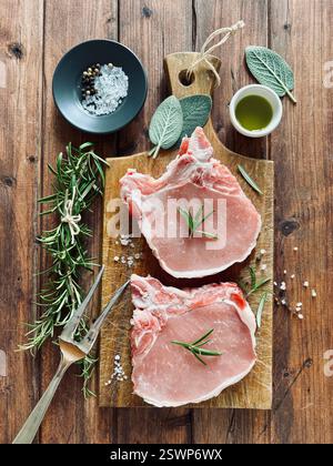 Rohe Schweinefleisch-Steaks auf dem Knochen und Kräuter auf einem hölzernen Schneidebrett. Frisches Schweinefleisch. Direkt darüber. Stockfoto