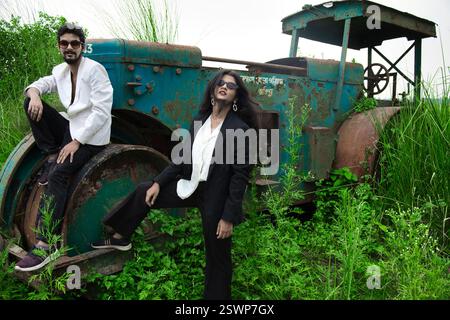 Models posieren auf offenem Feld vor einer alten Roadroller. Das Feld hat grünes Gras und sie sind in schwarz-weißen Anzügen gekleidet. Stockfoto