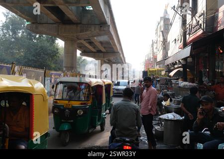 Autorikschas fahren auf einer belebten Straße in der Nähe des Bahnhofs Hazrat Nizamuddin in der indischen Hauptstadt Delhi an Straßenverkäufern vorbei Stockfoto