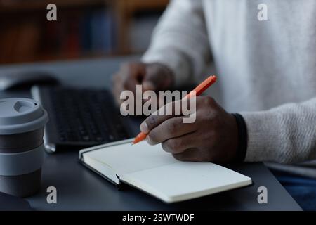 Nahaufnahme der Hand eines Schwarzen Mannes, der Notizen zum Schreiben auf Papier mit Stift im Notebook macht, um Arbeitsaufgaben am Schreibtisch im Büro und im Kopierraum zu verwalten Stockfoto