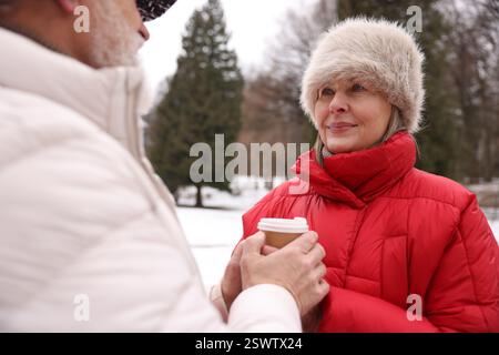 Nettes Seniorenpaar mit Pappbecher im Winterpark Stockfoto