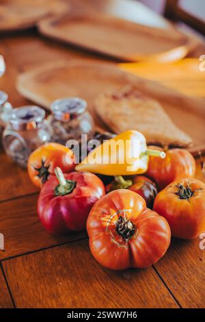 Verschiedene lebendige Tomaten und Paprika auf einem Holztisch in warmer Beleuchtung. Stockfoto