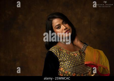 Mädchen in indischer Kleidung - schwarze Bluse und gelbe Lehenga und Dupatta schönes Make-up hält Blumen in der Hand auf schwarzem Hintergrund Stockfoto