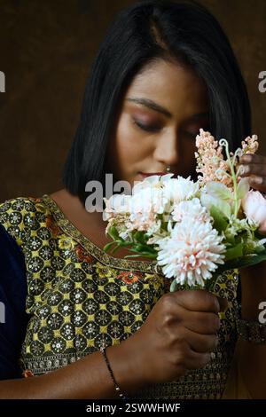Mädchen in indischer Kleidung - schwarze Bluse und gelbe Lehenga und Dupatta schönes Make-up hält Blumen in der Hand auf schwarzem Hintergrund Stockfoto