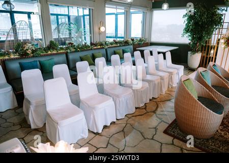 Ein elegantes und ruhiges Ambiente für eine Hochzeitszeremonie. Reihen von weißen Stühlen zeigen nach vorne und sind für Gäste bereit. Der Innenraum ist mit bota ausgestattet Stockfoto