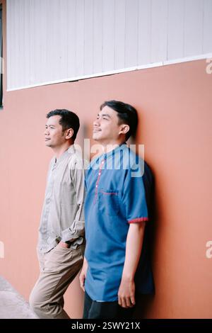 Zwei asiatische Männer in lässiger Kleidung stehen nebeneinander an einer Korallenwand. Sie blicken in die Ferne und teilen einen ruhigen Moment der Besinnung Stockfoto