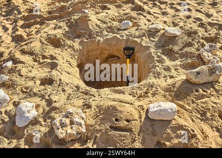 Malta - 4. Dezember 2023: Eine Sandgrube mit einer Schaufel am Strand, umgeben von Steinen. Ein lächelndes Gesicht wird in den Sand gezeichnet. Die Szene zeigt eine kreative Freizeitaktivität in einer sonnigen Küstenlandschaft *** eine Sandgrube mit einer Schaufel am Strand, umgeben von Steinen. Im Sand ist ein lächelndes Gesicht gezeichnet. Die Szene zeigt eine kreative Freizeitaktivität in einer sonnigen Küstenlandschaft Stockfoto