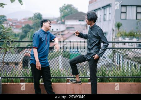 Zwei junge Männer unterhalten sich entspannt auf einer Dachterrasse. Sie sind lässig gekleidet und genießen die Gesellschaft des anderen. Das urbane Stadtbild Stockfoto