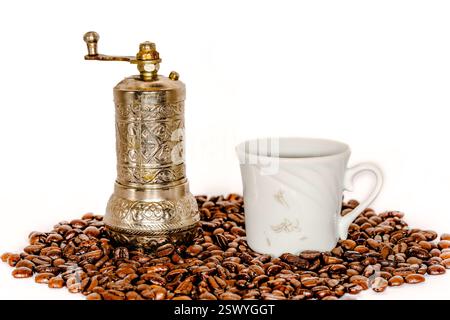 Vintage-Handkaffeemühle mit kunstvollem Metalldesign und weißer Porzellanschale auf gerösteten Kaffeebohnen Stockfoto