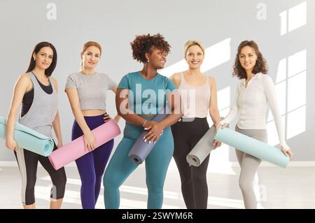 Gruppe von sportlichen Multi-ethnischen Mädchen, die Yogamatten halten, Yoga üben, Fitnessunterricht, Trainer Stockfoto