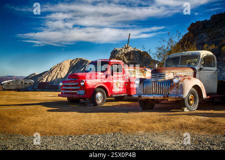 Zwei alte LKW stehen auf einem Schotterfeld. Einer ist rot und der andere weiß. Der rote Truck ist ein Chevrolet und der weiße Truck ein Ford Stockfoto