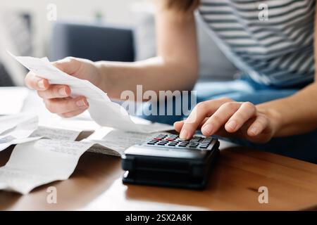 Junge Frau, die Haushaltssteuerrechnungen und -Ausgaben kalkuliert und zu Hause auf dem Sofa sitzt Stockfoto