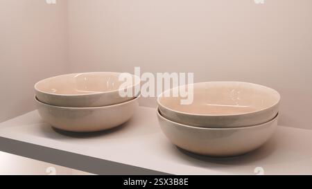 Drei weiße Schüsseln sitzen auf einem Regal. Die Schüsseln haben alle die gleiche Größe und Form, und sie sind alle weiß. Die Szene ist einfach und unübersichtlich Stockfoto