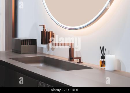 Ein Waschbecken im Badezimmer mit einem goldenen Wasserhahn und einem Seifenspender. Eine Kerze steht auf dem Tresen neben dem Waschbecken Stockfoto