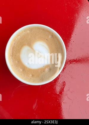 Tasse Cappuccino mit herzförmiger Latte Art auf einem roten Tisch Stockfoto