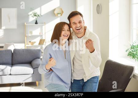 Glückliches überglücktes junges Paar, das zu Hause im Wohnzimmer steht. Stockfoto
