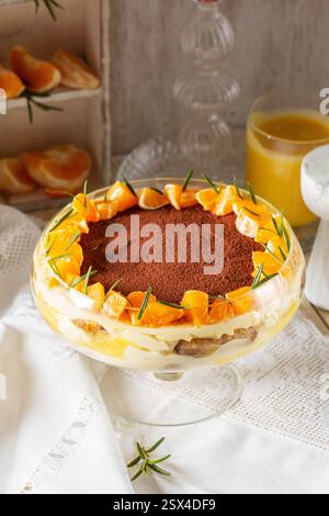 Tiramisu-Dessert mit Mascarponcreme und Zitronen-Mandarinen-Quark. Traditionelles italienisches Dessert, dekoriert mit Kakao, Mandarinenscheiben und Rosmarin auf einem li Stockfoto