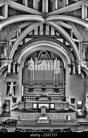Das Bild ist ein Schwarzweißfoto einer Kirche mit einer großen Orgel. Die Orgel ist der Hauptfokus des Bildes und ist von Bänken und einem Choi umgeben Stockfoto