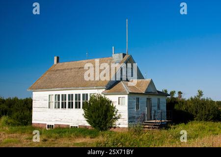 Kleines, altes weißes Haus mit schrägem Dach auf einem Feld. Das Haus ist von Gras und Bäumen umgeben, und der Himmel ist klar und blau. Das Haus Appa Stockfoto