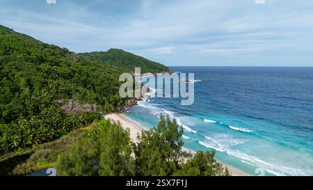 Tropischer Strand mit türkisfarbenen Wellen, weißem Sand und grünen Hügeln im Hintergrund. Seychellen, Mahe. Anse Petit Boileau. Stockfoto