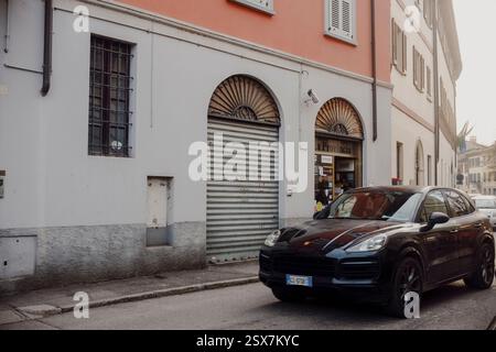 Cremona, Italien, 9. Februar 2025 Schwarzer Porsche Cayenne, der an einem Zeitungskiosk in den bezaubernden Straßen von Cremona, Italien vorbeifährt und den Luxus und das Our hervorhebt Stockfoto