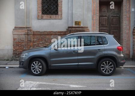 Cremona, Italien 9. Februar 2025 moderner, grauer Volkswagen Tiguan parkt neben einer Backsteinmauer und einer alten Holztür in Cremona, Italien Stockfoto