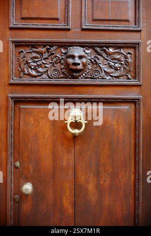 Cremona, Italien, 9. Februar 2025 Alte hölzerne Eingangstür mit Löwenkopf-Flachrelief, Messingklopfer und Griff in Cremona, Italien Stockfoto