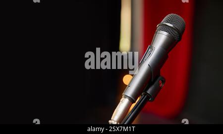 Ein Mikrofon befindet sich auf einem stabilen Ständer vor einem eleganten roten Vorhang und ist bereit, in dieser lebendigen Umgebung Sound aufzunehmen. Ein Banner für Stockfoto
