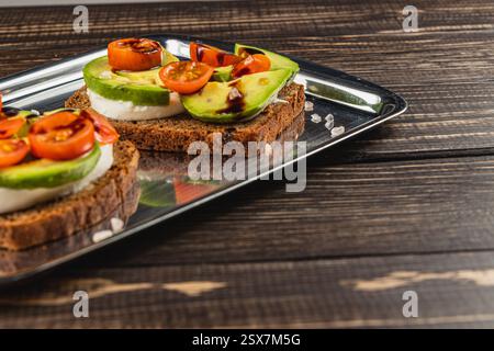 Frisch zubereitete Sandwiches mit offenem Gesicht werden auf einem Metalltablett serviert, mit knusprigem Brot, cremigem Käse, geschnittener Avocado, Kirschtomaten, Stockfoto