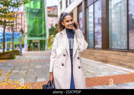 Afrikanische Geschäftsfrau, die im Herbst mit gefallenem Laub mit dem Mobiltelefon auf einer Stadtstraße spricht Stockfoto