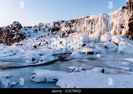 Winterszene im Freien mit einem schneebedeckten Fluss in der Nähe des teilweise gefrorenen Oxararfoss Wasserfalls im Thingvellir Nationalpark im Goldenen Kreis in Island. Stockfoto