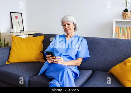 Leitende Pflegekraft, die sich nach dem Arbeitstag auf dem Sofa mit dem Mobiltelefon entspannt Stockfoto