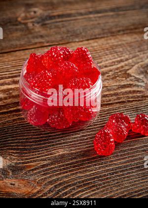 Himbeerförmige Süßigkeiten in einem klaren Glas. Brauner Holzhintergrund. Stockfoto
